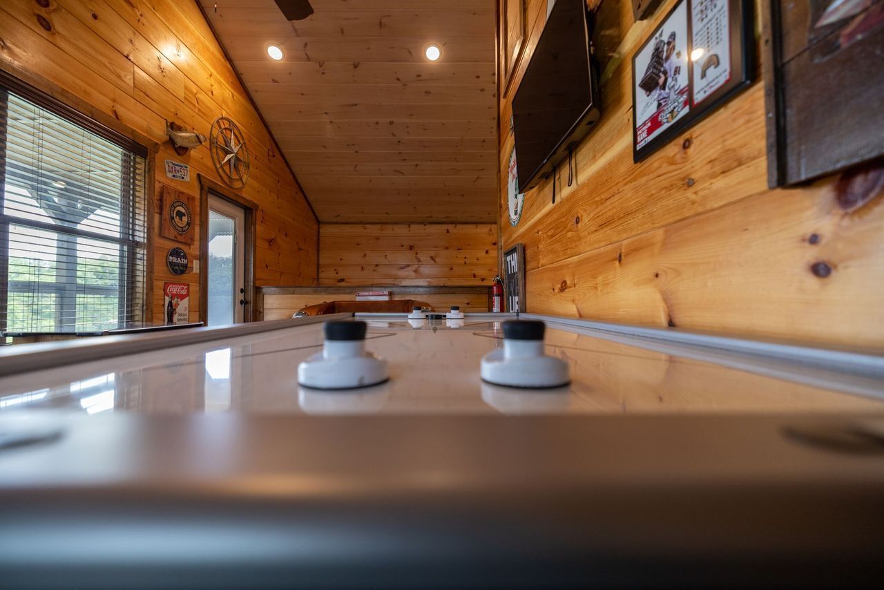 Ein Shuffleboardtisch in einem Holzraum mit einem an der Wand befestigten Fernseher und verschiedenen Wandschildern.