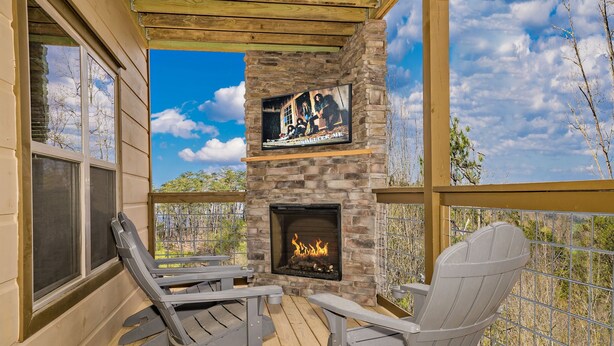 Un espace extérieur aménagé, abrité et doté d’une cheminée en pierre, d’une terrasse en bois et de fauteuils Adirondack.