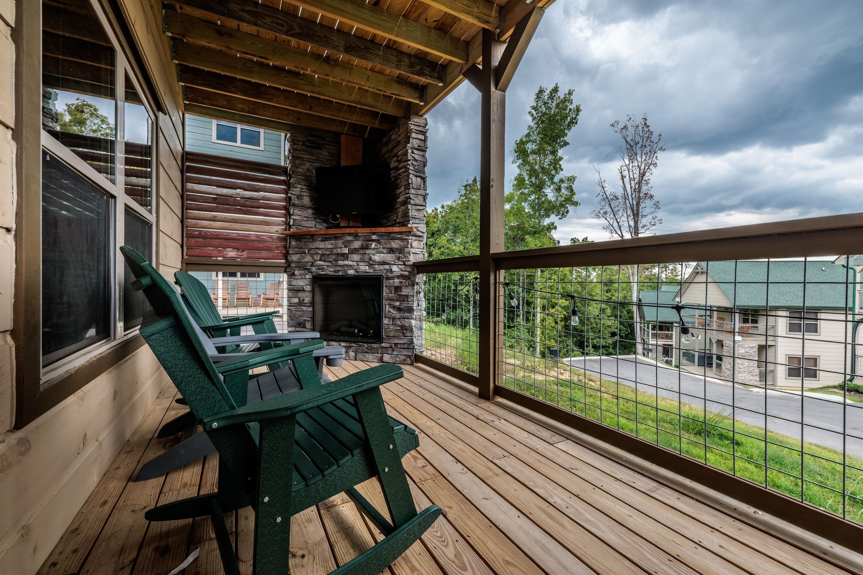 Une terrasse couverte avec une cheminée en pierre et des fauteuils Adirondack verts.