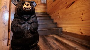 Une sculpture d’ours en bois se trouve dans un couloir aux murs en bois, près d’un escalier.