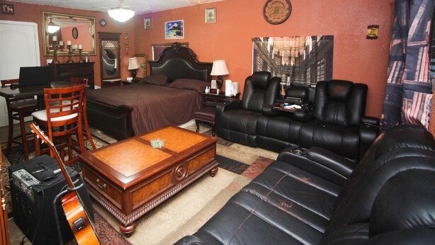 Una habitación con una cama, un sofá, una mesa de centro, un escritorio con una silla, una guitarra y una lámpara.
