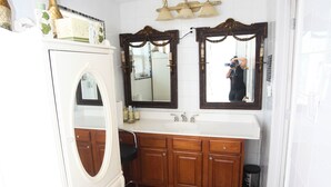 Un baño con tocador blanco, armarios de madera, un espejo grande y un banco negro.