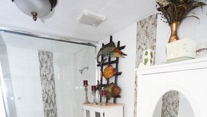 Un baño con ducha de vidrio, inodoro blanco, tocador con espejo y alfombra estampada.