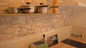 A kitchen with a stone wall, a shelf with pots, a toaster, and a wooden spoon holder. - Hideaway gite for 2 with private garden and sundeck, close to Atlantic beaches. (Épargnes)
