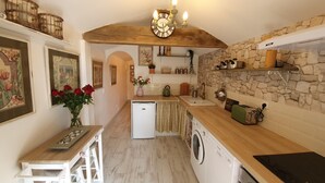 A compact kitchen with a stone wall, wooden beams, a built-in washing machine, and a small refrigerator. - Hideaway gite for 2 with private garden and sundeck, close to Atlantic beaches. (Épargnes)
