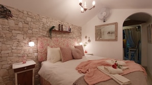 A bedroom with a stone wall, a bed with pink bedding, a bedside table with a lamp, and a mirror on the wall. - Hideaway gite for 2 with private garden and sundeck, close to Atlantic beaches. (Épargnes)