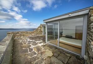 A modern room with a stone exterior and a glass wall, overlooking a body of water. - Romantic Castle at Roaring Water Bay in West Cork  -  Weekend special available (Skibbereen)