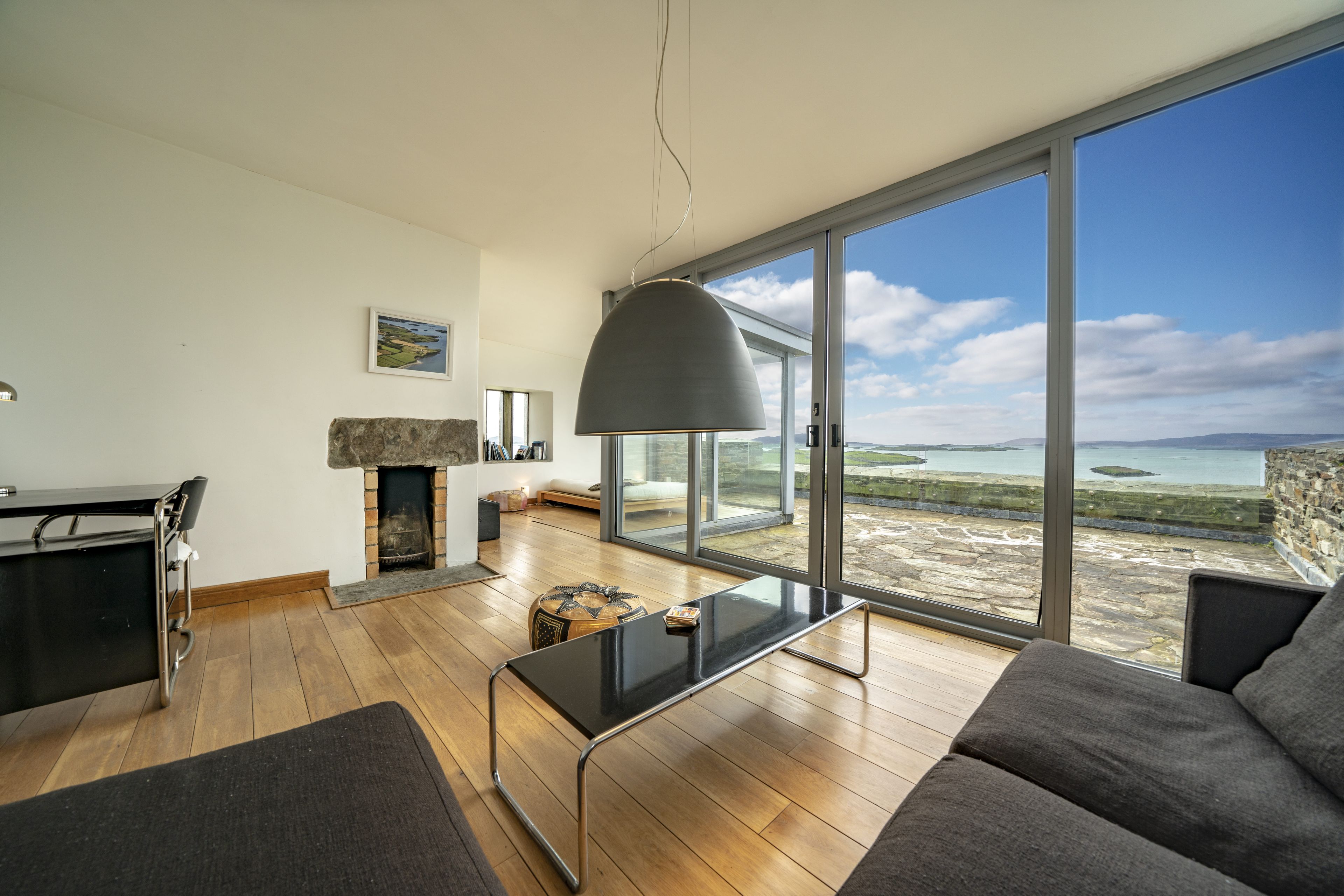 Un salon moderne doté d’une cheminée, d’un coin repas et d’une grande fenêtre offrant une vue sur la mer.