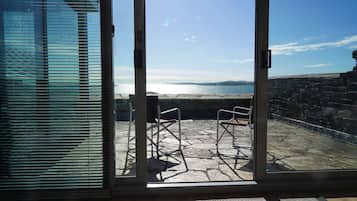 On aperçoit, à travers une porte vitrée, un patio extérieur doté d’un sol en pierre et de deux chaises en métal.