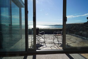 A view through a glass door to an outdoor patio with stone flooring and two metal chairs.