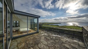 A modern glass-walled bedroom with a view of the sea and a stone terrace. - Romantic Castle at Roaring Water Bay in West Cork  -  Weekend special available (Skibbereen)