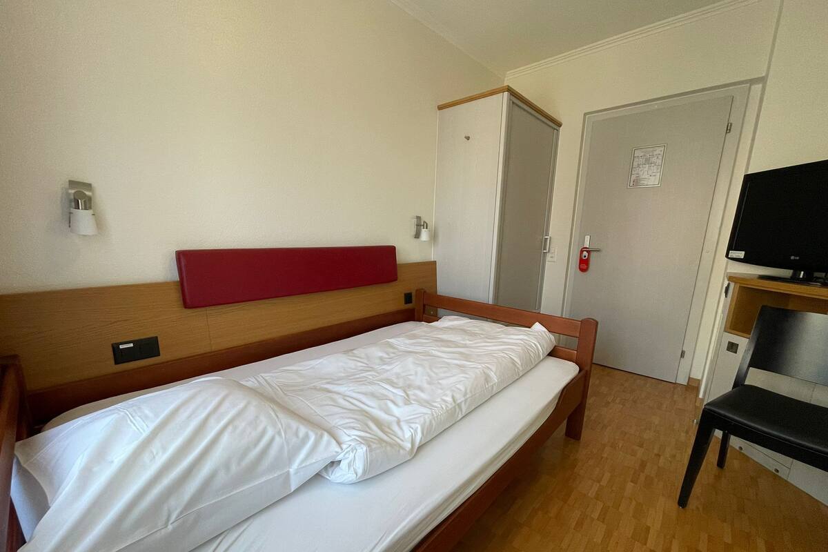 A single bed with a wooden headboard and white bedding in a room with a wooden floor.