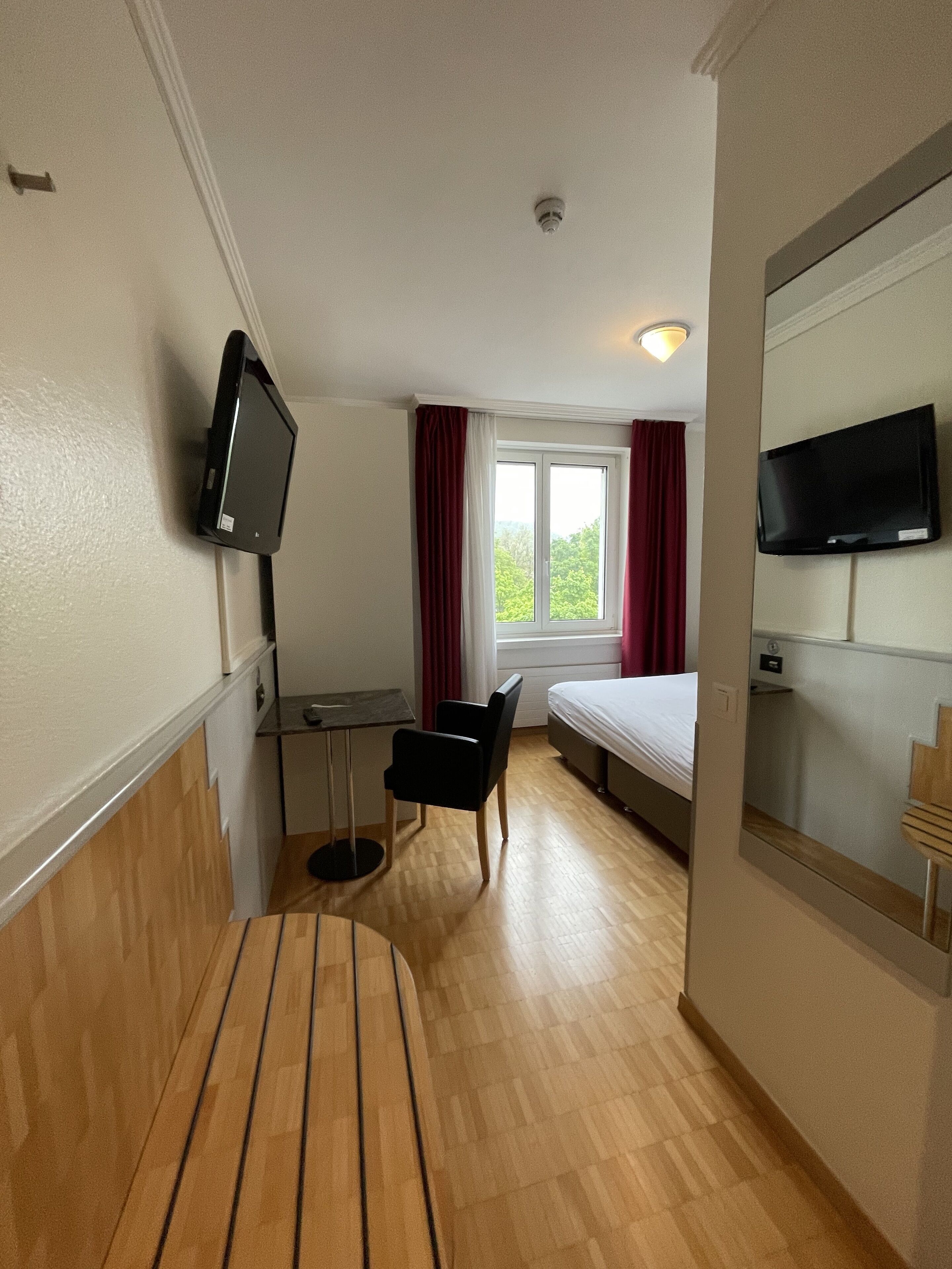 Habitación de hotel con cama, escritorio, silla, televisión y ventana con cortinas.