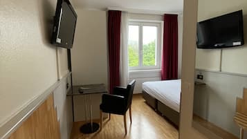 A hotel room with a bed, a desk, a chair, a TV, and a window with curtains.