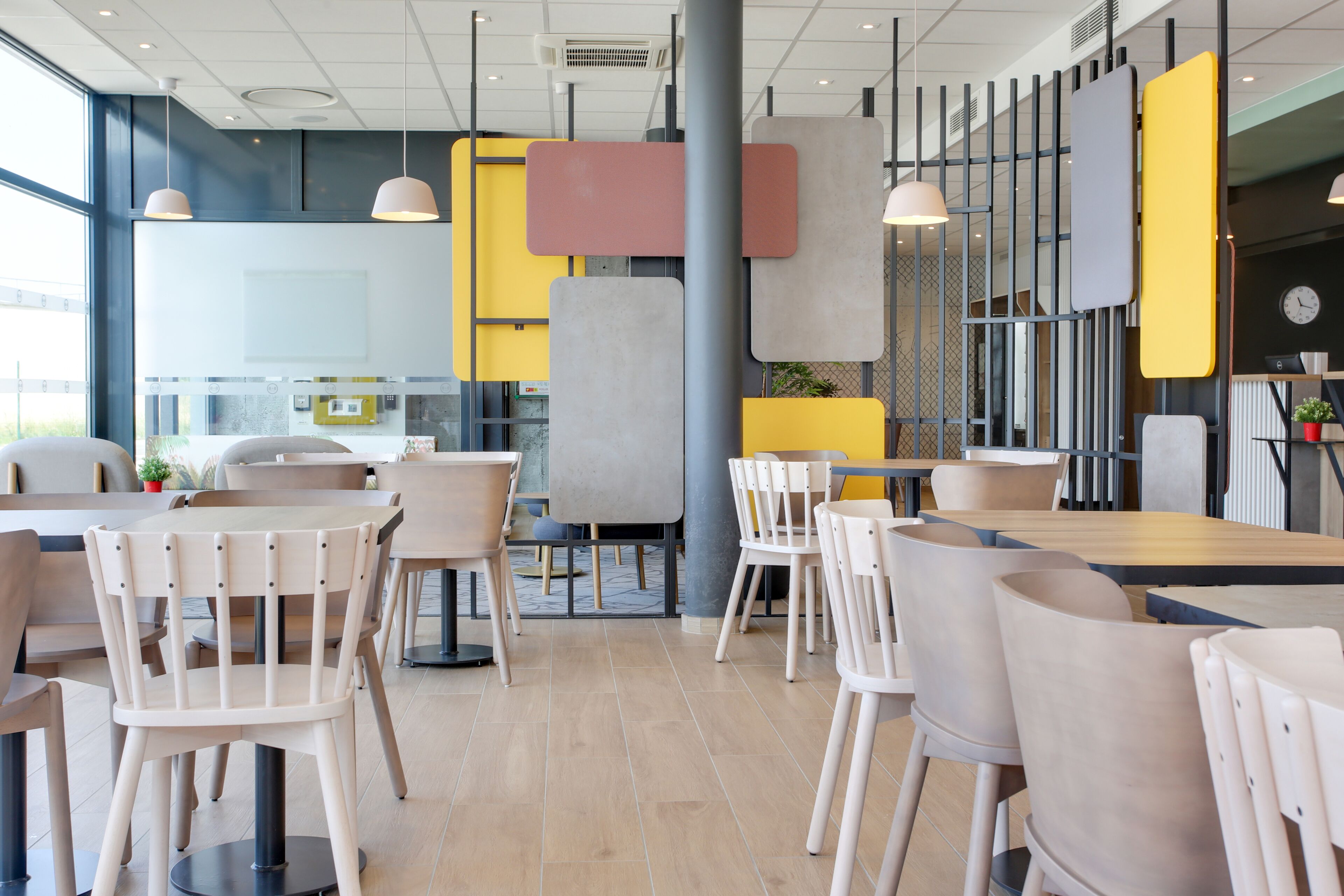 A modern restaurant interior with multiple seating areas, including round tables and chairs, and a visible kitchen area in the background.