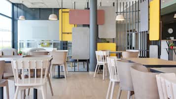 Un intérieur de restaurant moderne avec plusieurs espaces de restauration, comprenant des tables et des chaises rondes, et une cuisine ouverte visible au fond.