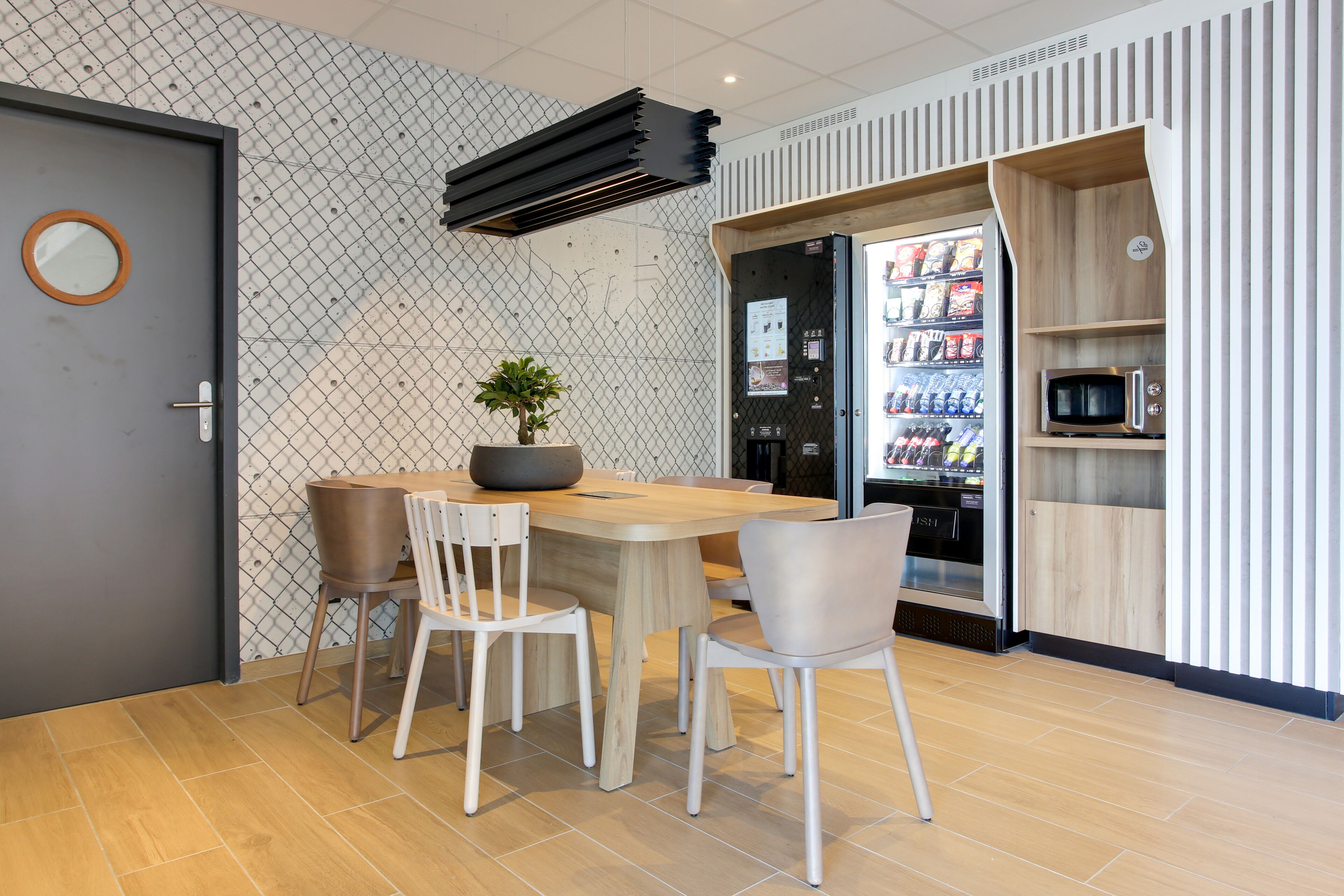 A modern dining area with a wooden table and chairs, a potted plant, and a refrigerator stocked with beverages.
