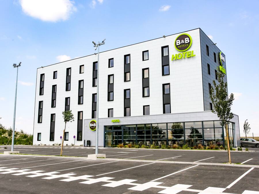 A modern B&B hotel with a white facade, large windows, and a parking lot.