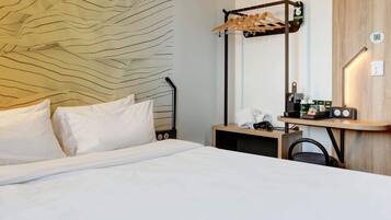 A hotel room with a bed, a wooden headboard, a mirror, a side table with a radio, and a coat rack.