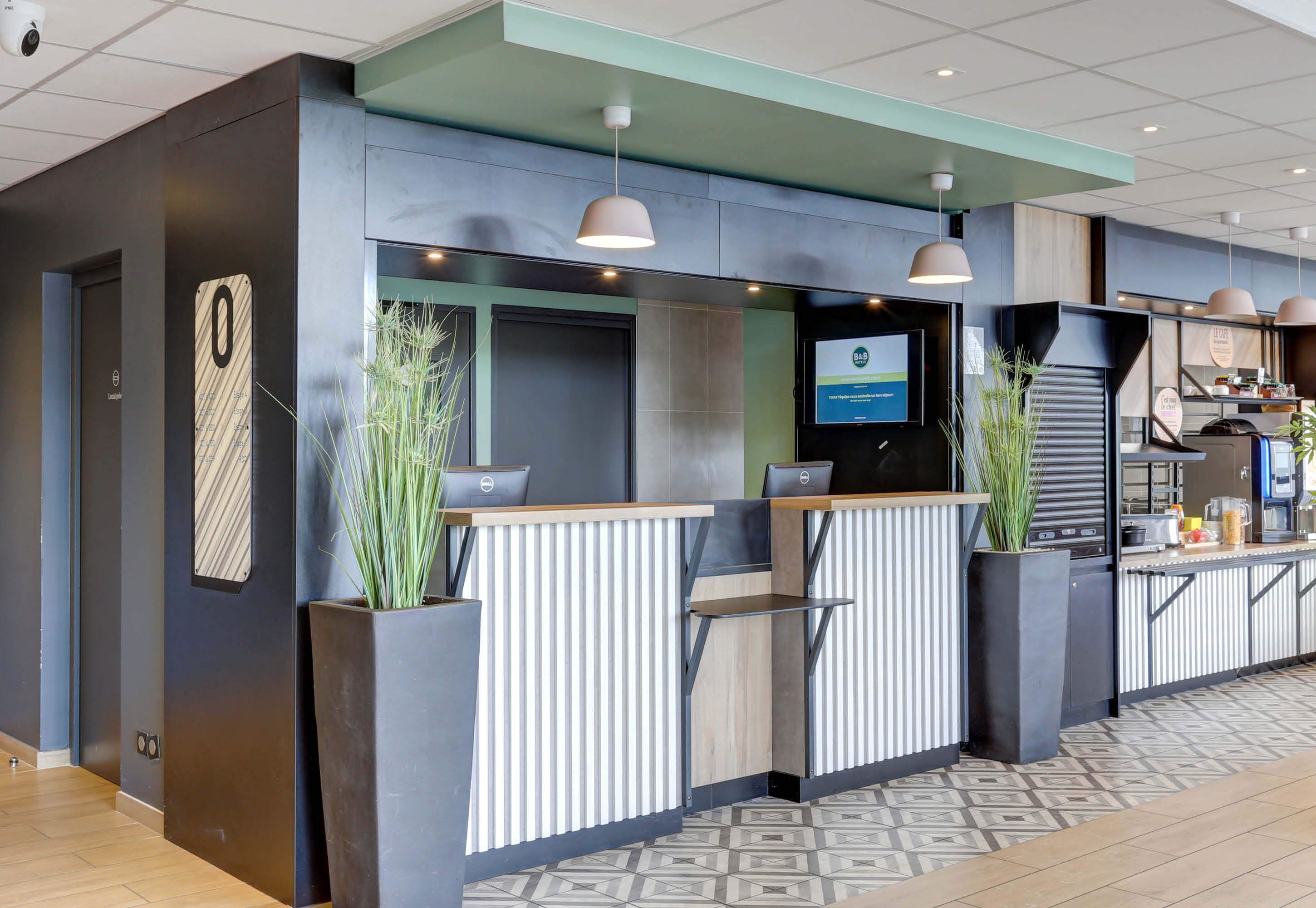 A reception area with a modern design, featuring a reception desk, a digital screen, and potted plants.