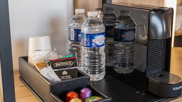 Escritorio de hotel con cafetera, dos botellas de agua, azúcar en caja y bombones.