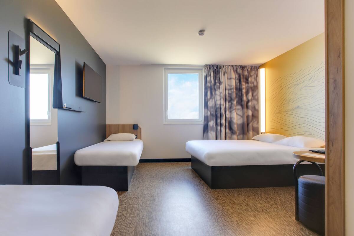 A hotel room with two beds, a TV, a window, and a curtain.