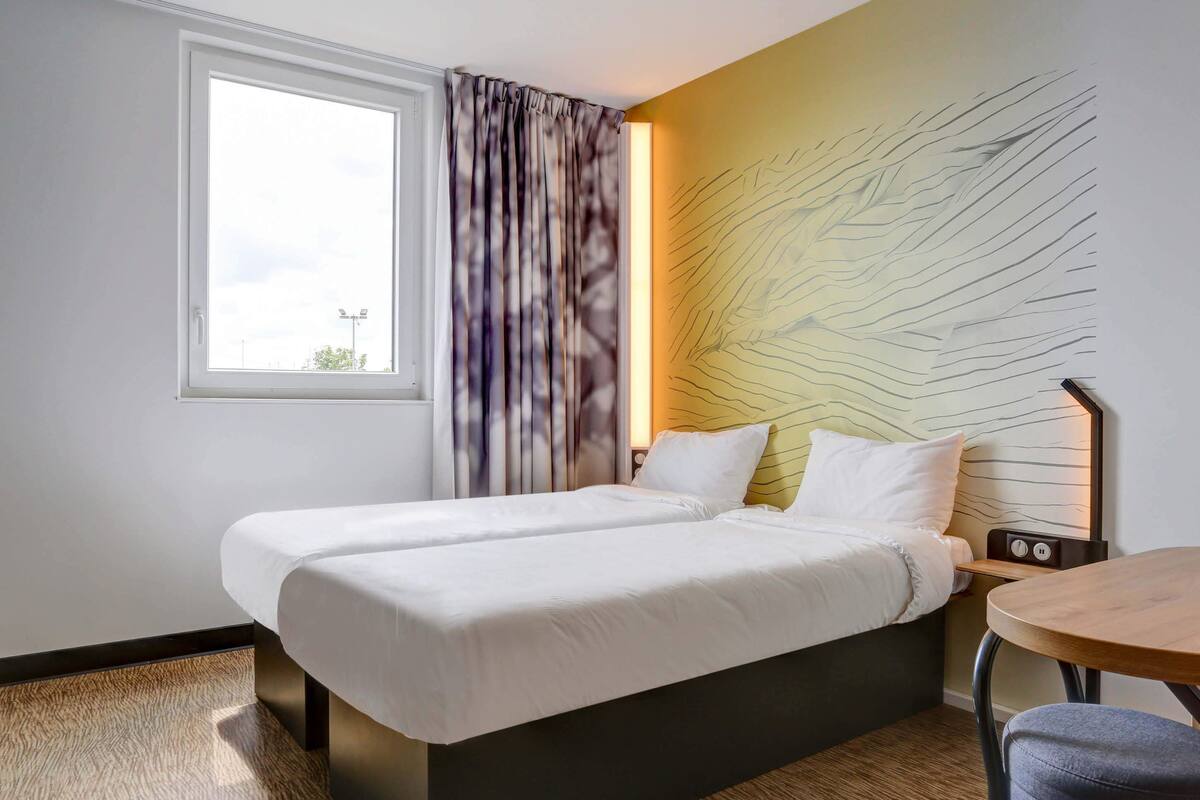A hotel room with a bed, a small table, and a window with curtains.