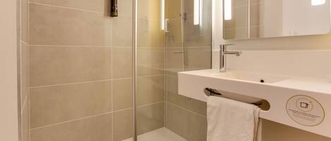 Une salle de bain moderne avec une douche à parois de verre, un lavabo blanc et une serviette accrochée au mur.