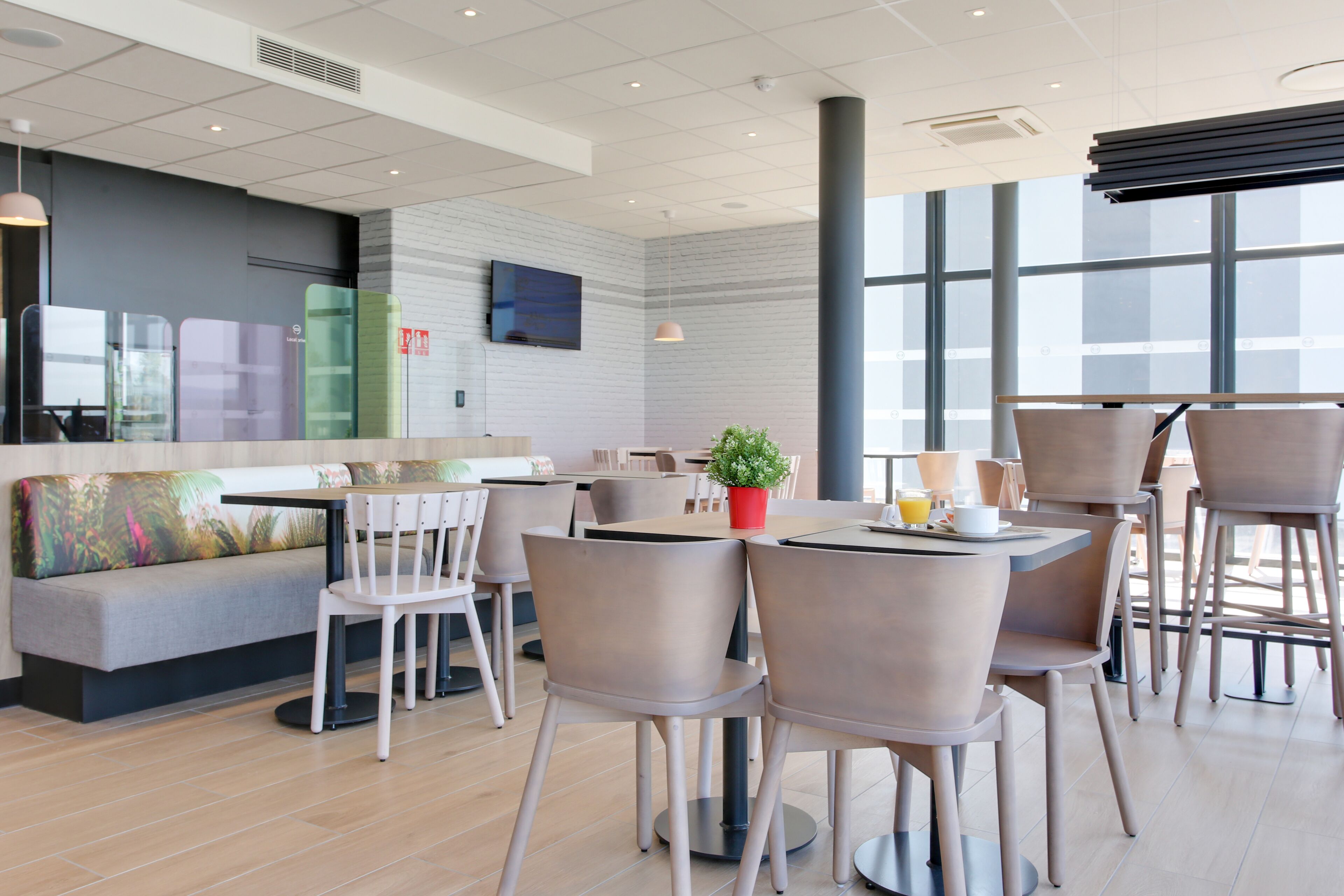 Un café moderne doté d’une grande fenêtre, d’un téléviseur à écran plat et de différents types de sièges, notamment des tables et des chaises.