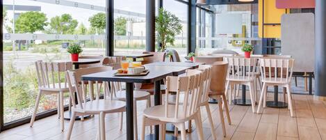 Un restaurant moderne doté de grandes fenêtres, de tables et de chaises en bois, et agrémenté de plantes en pot.