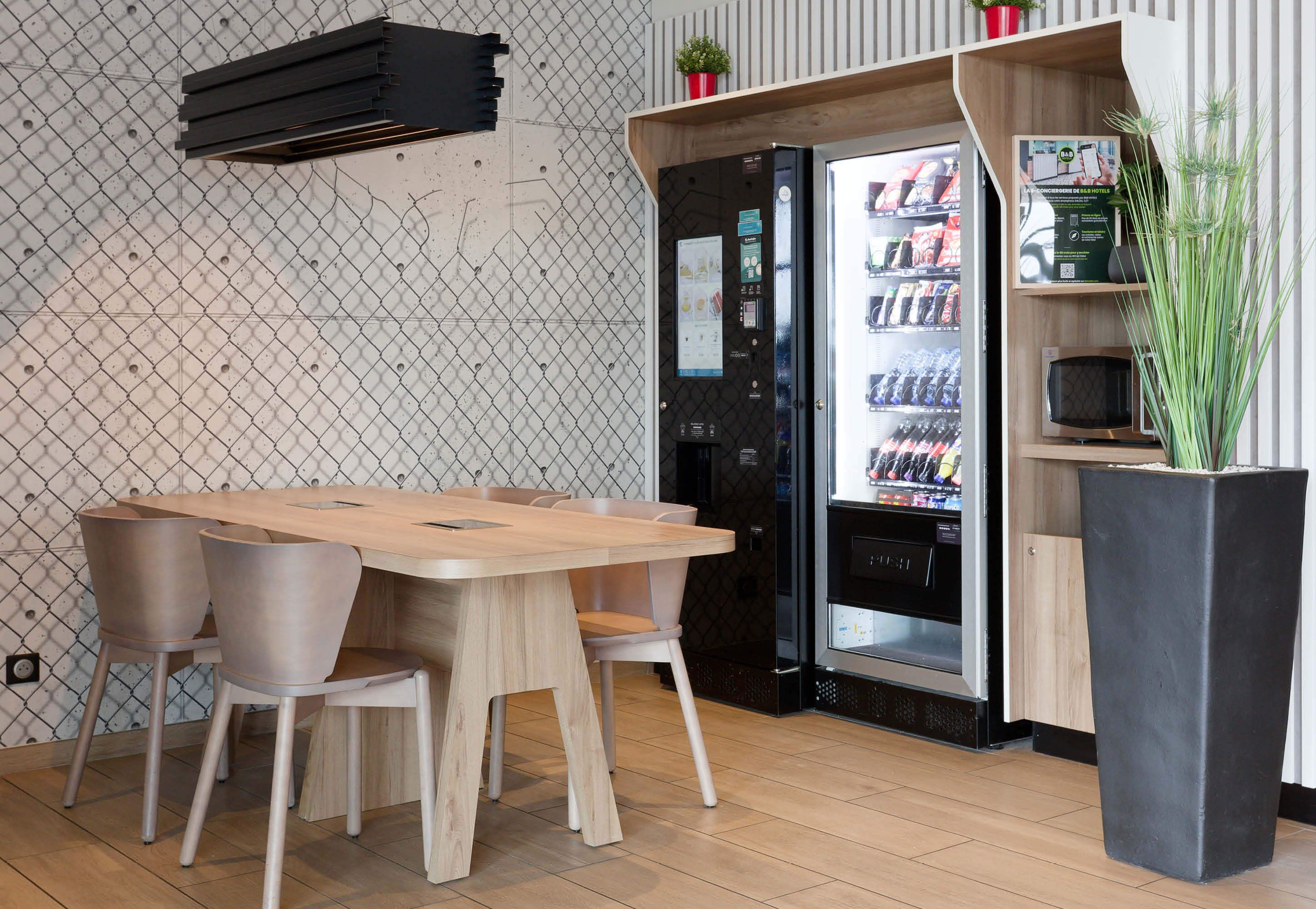 A modern kitchen with a wooden table and chairs, a refrigerator stocked with beverages, and a microwave on a shelf.