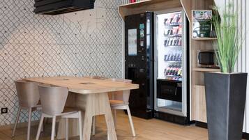A modern kitchen with a wooden table and chairs, a refrigerator stocked with beverages, and a microwave on a shelf.