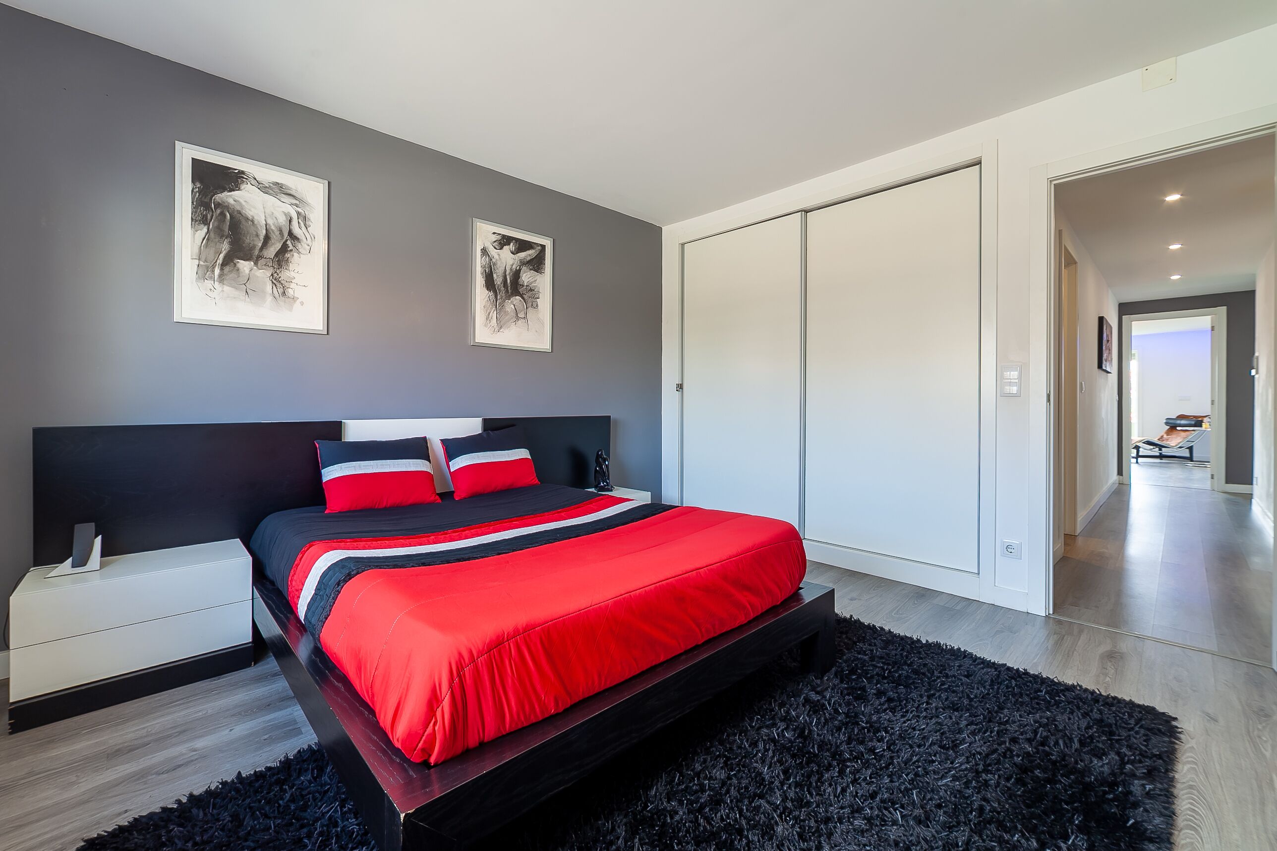 A modern bedroom with a large bed, a nightstand, a black rug, and two framed pictures on the wall.
