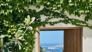 Vista a través de un marco de madera a un balcón con silla y mesa, con vistas al paisaje costero.
