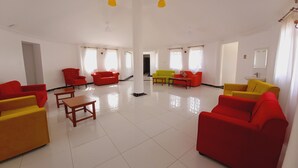 A spacious living area with multiple red and yellow sofas, a wooden coffee table, and a bright, well-lit room with large windows. - Athi Holiday Resort (Athi River)