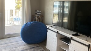 Una sala de estar con un televisor de pantalla plana grande, un sillón inflable azul, un mueble blanco para entretenimiento y vistas al exterior a través de un puertas correderas de vidrio.
