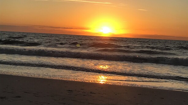Un atardecer sobre el océano con olas acercándose a la orilla.