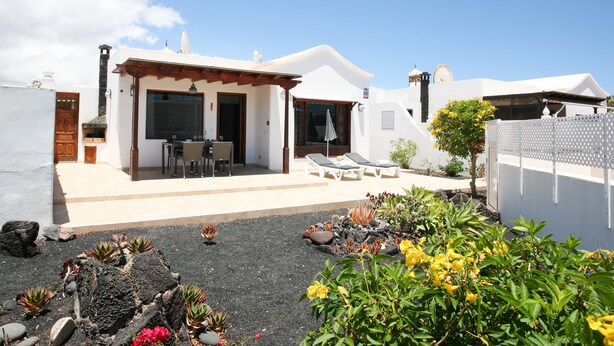 Une maison moderne dotée d’un patio, d’un espace salon extérieur et d’un jardin agrémenté de diverses plantes et fleurs.
