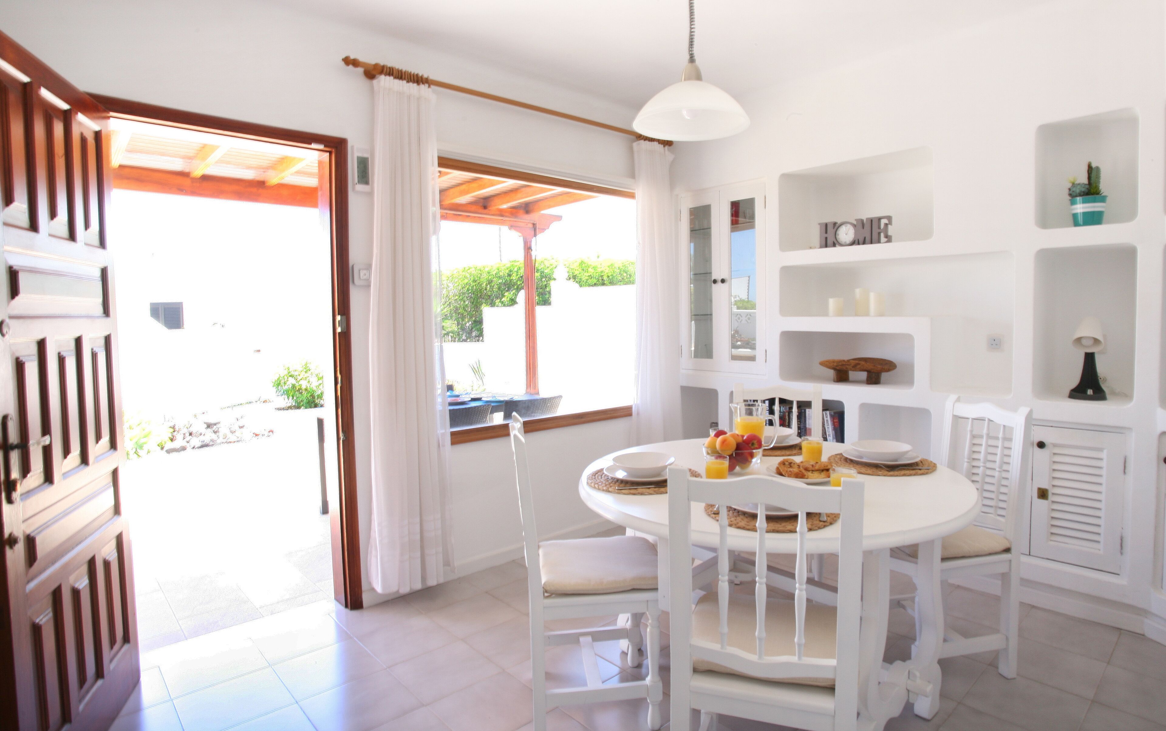 A bright dining area with white furniture, a round table, and a view of the outdoors through a window.