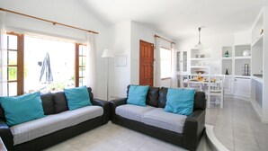 Un salon moderne avec deux canapés sombres, des coussins turquoise et une table à manger blanche avec des chaises.