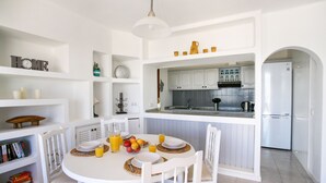 Une cuisine moderne avec des meubles blancs, une table à manger dressée avec des assiettes, des verres et un panier de fruits.