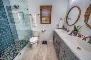 A bathroom with a glass shower enclosure, a toilet, a vanity with a sink, and a window with blinds.