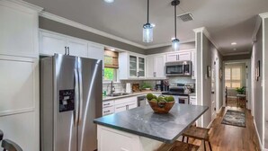 A modern kitchen with stainless steel appliances, white cabinetry, and a central island with stools. - DT 430 Momma's House on Landa (New Braunfels)