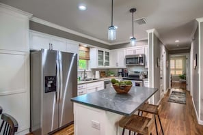 A modern kitchen with stainless steel appliances, white cabinetry, and a central island with stools.