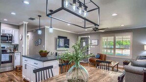 A modern kitchen with a central island, a dining area with a wooden table, and a living room with a sofa. - DT 430 Momma's House on Landa (New Braunfels)