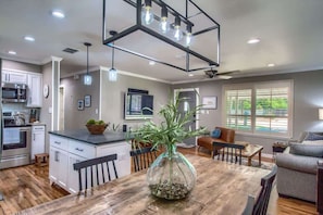 A modern kitchen with a central island, a dining area with a wooden table, and a living room with a sofa.
