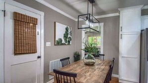 A dining area with a wooden table, chairs, a hanging light fixture, and a potted plant. - DT 430 Momma's House on Landa (New Braunfels)
