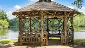 A wooden gazebo with a hexagonal roof and lattice design, situated by a lake. - DT 430 Momma's House on Landa (New Braunfels)