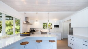 Una cocina moderna con armarios blancos, una isla grande con taburetes de bar y vistas al exterior.