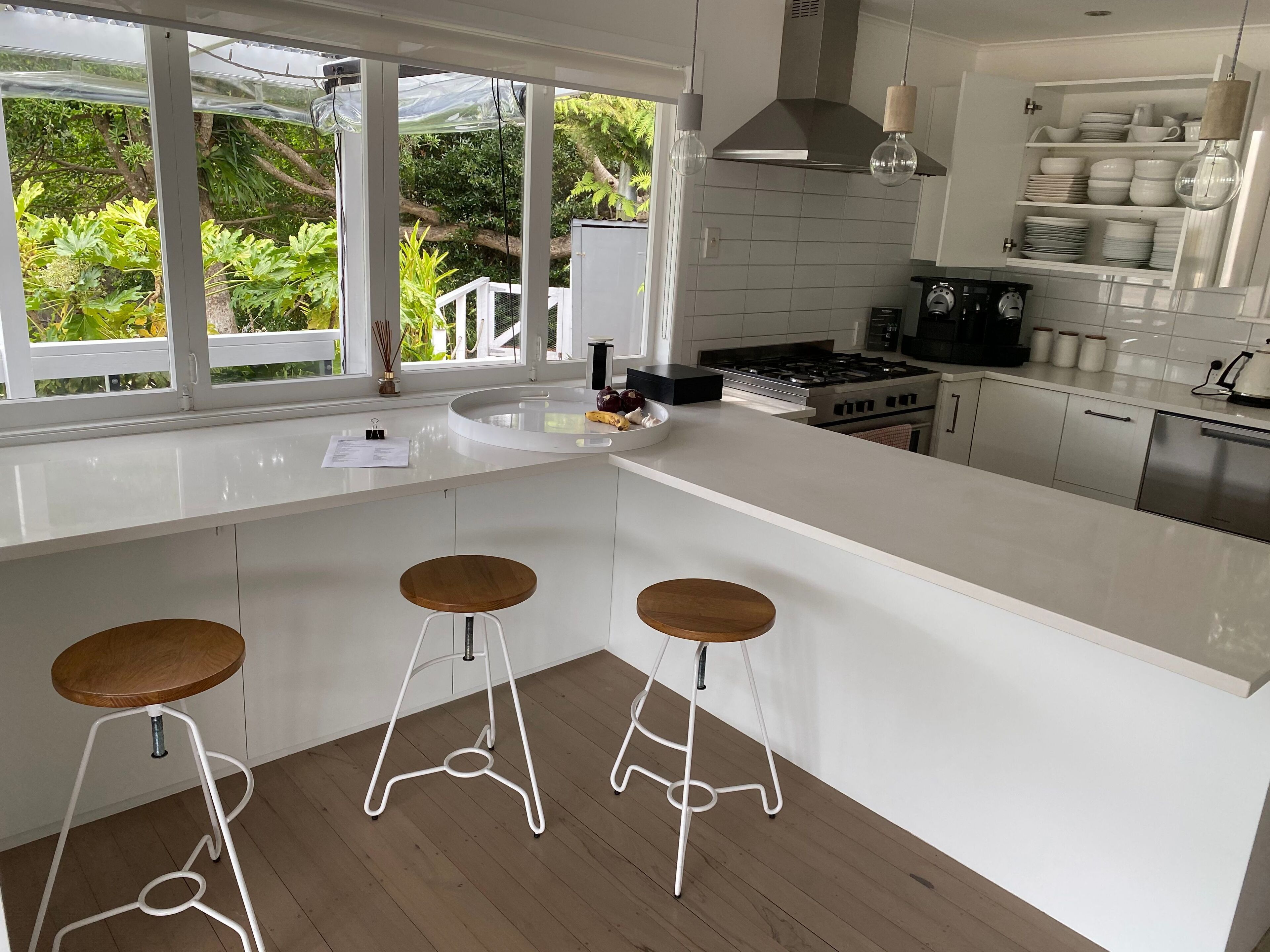 Cocina moderna con encimeras blancas, cocina a gas y un amplio ventanal con vistas a la vegetación.